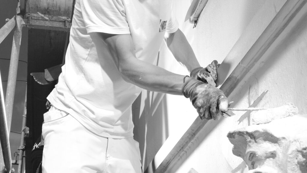 Schwarz-Weiß-Aufnahme von Handwerkern, die Holzrahmen abschleifen, möglicherweise Fensterrahmen oder Türen.