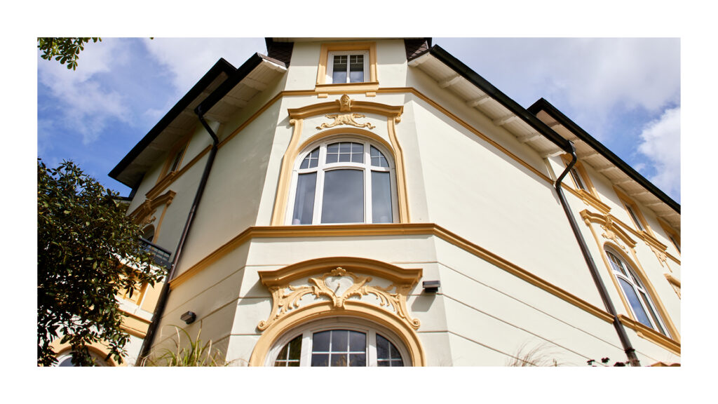 Nahaufnahme eines architektonischen Details der Fassade: eine helle Gebäudeecke mit dekorativen Stuckelementen und einem Erkerfenster.