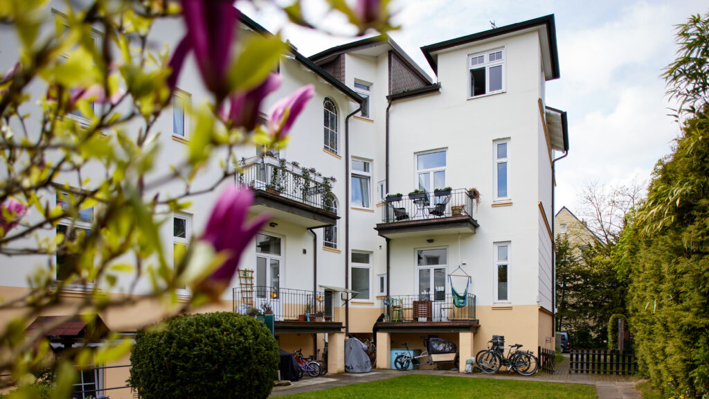 Außenansicht des sanierten Altbaus aus einem anderen Blickwinkel, mit Balkonen und einem blühenden Magnolienzweig im Vordergrund.
