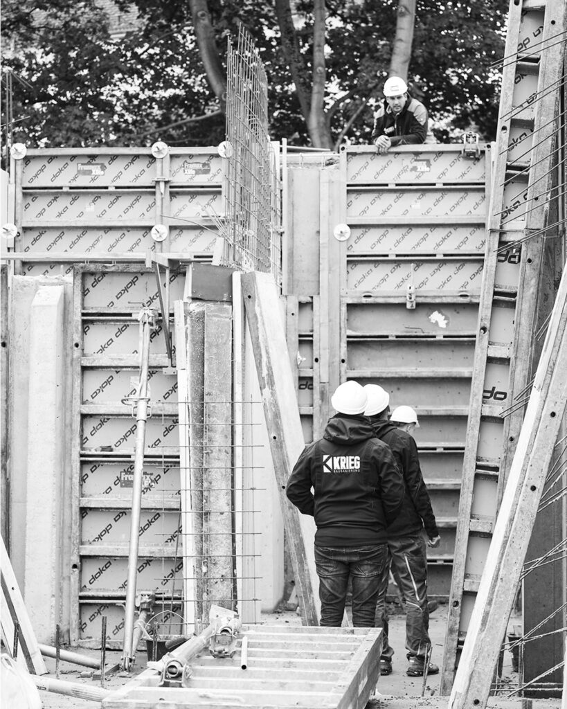 Bauarbeiter des Teams Bausanierung Krieg in Arbeitskleidung bei der präzisen Montage von Wandschalungen für das Verblendmauerwerk des Rohbaus.