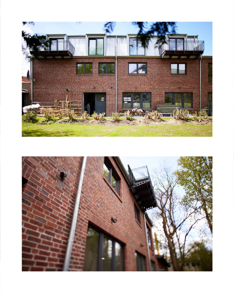 Rückansicht des Neubaus mit hochwertigem rotem Klinkermauerwerk, großen Fensterausschnitten und fertig montierten Balkonanlagen im Obergeschoss.