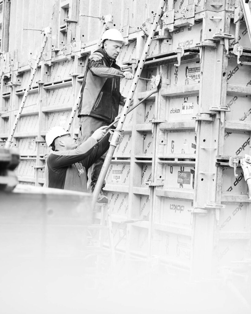 Facharbeiter auf einer Leiter bei der Sicherung der Schalungselemente für die massiven Stahlbetonwände des Projekts.