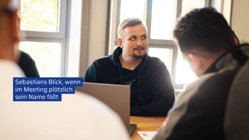 Ein Mitarbeiter von KRIEG Bausanierung in einer authentischen Meetingsituation. Er schaut schmunzelnd zur Seite, während er an einem Laptop sitzt. Das Bild enthält einen humorvollen Text über Meetings und das Firmenlogo in der unteren linken Ecke.