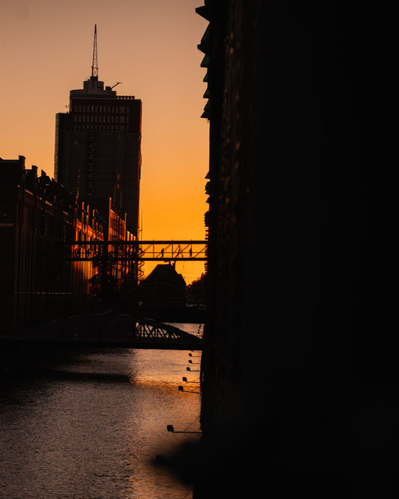 Speicherstadt Hamburg Silhouette Sonnenuntergang: Backsteingebäude, Fleet, Kehrwiedersteg, Brücke mit Personen, im Hintergrund der Fernsehturm-Turm.