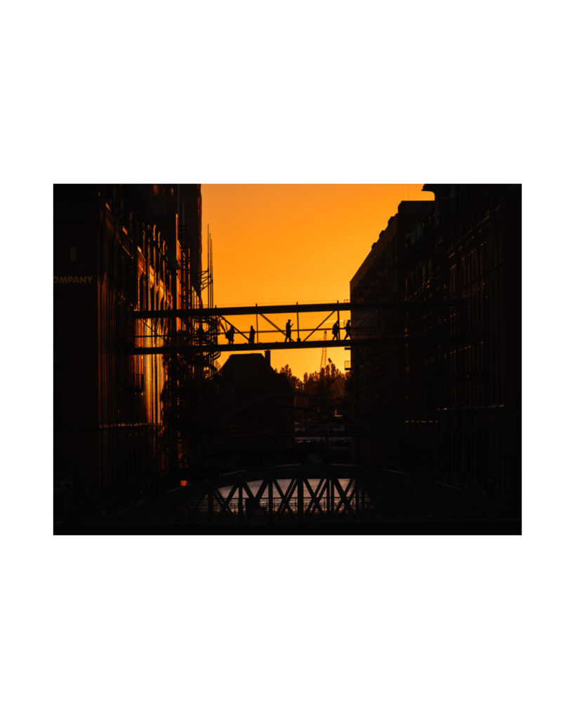 Detaillierter Sonnenuntergang Hamburg Speicherstadt: Nahaufnahme von Backsteingebäuden, die einen Fleet säumen, mit dem Kehrwiedersteg und Silhouetten von Fußgängern auf der Brücke.