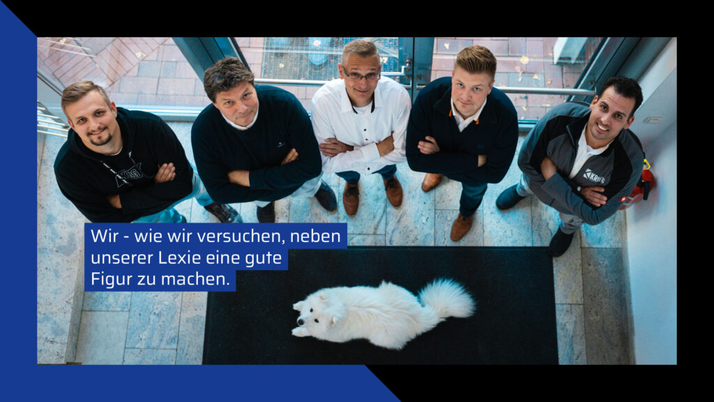 Team der Krieg Bausanierung mit Bürohund Lexie: Fünf Mitarbeiter in Business-Pose und ein weißer flauschiger Hund in der Draufsicht. Sympathisches Teambild der Experten für Sanierung und Renovierung zur Darstellung der Unternehmenskultur.