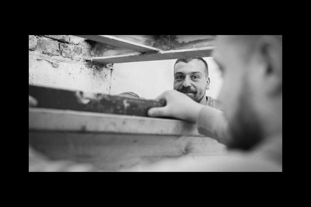 Nahaufnahme in Schwarz-Weiß von zwei Handwerkern auf einer Baustelle bei der präzisen Arbeit mit einer Wasserwaage an einem Holzbalken.