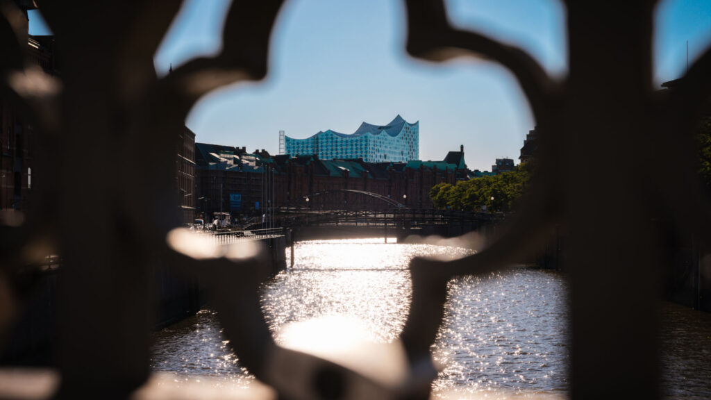 Blick auf die Elbphilharmonie durch ein Brückengitter in der Hamburger Speicherstadt im Sommer