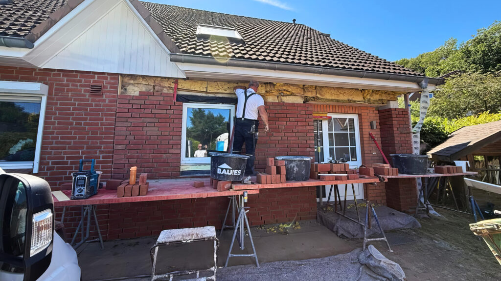 Handwerker setzt präzise rote Verblendklinker an der gedämmten Außenwand eines Wohnhauses