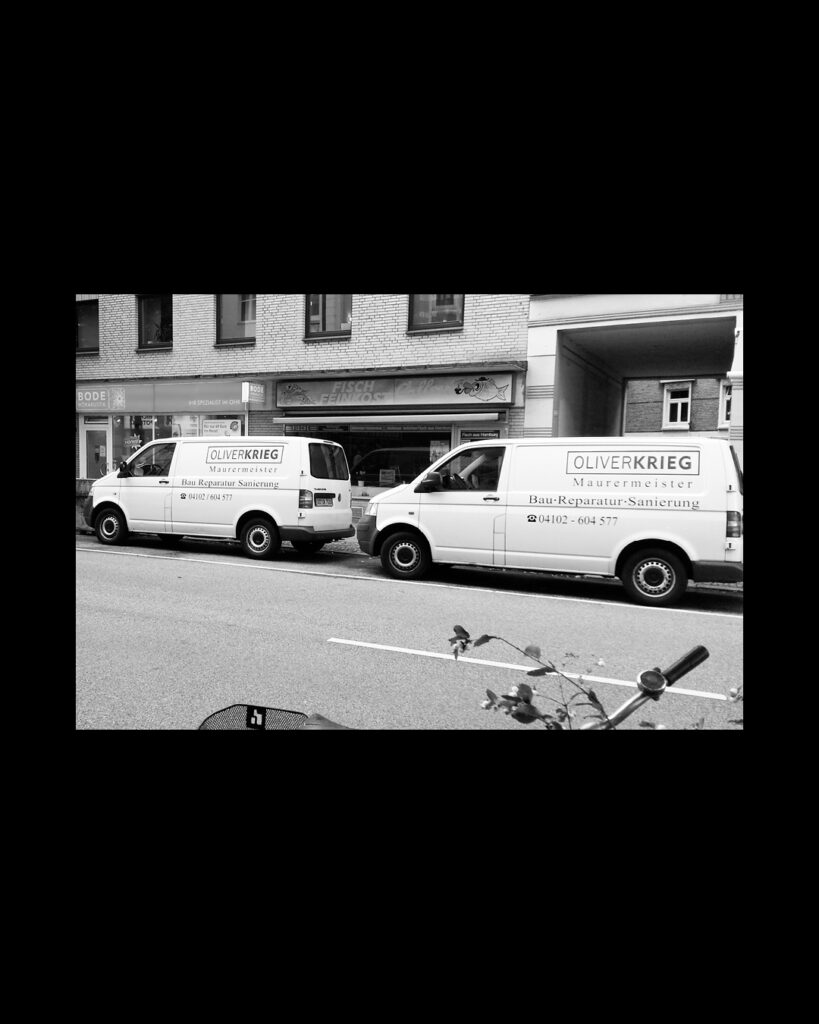 Schwarz-Weiß-Foto von zwei Firmenfahrzeugen der Oliver Krieg Bausanierung, geparkt an einer Hamburger Straße vor Gewerbegeschäften.   
