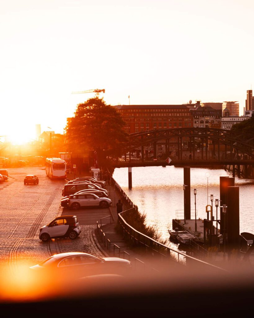 Kanal und stählerne Brücke in der Hamburger Speicherstadt im goldenen Sonnenuntergangslicht mit parkenden Autos am Kai